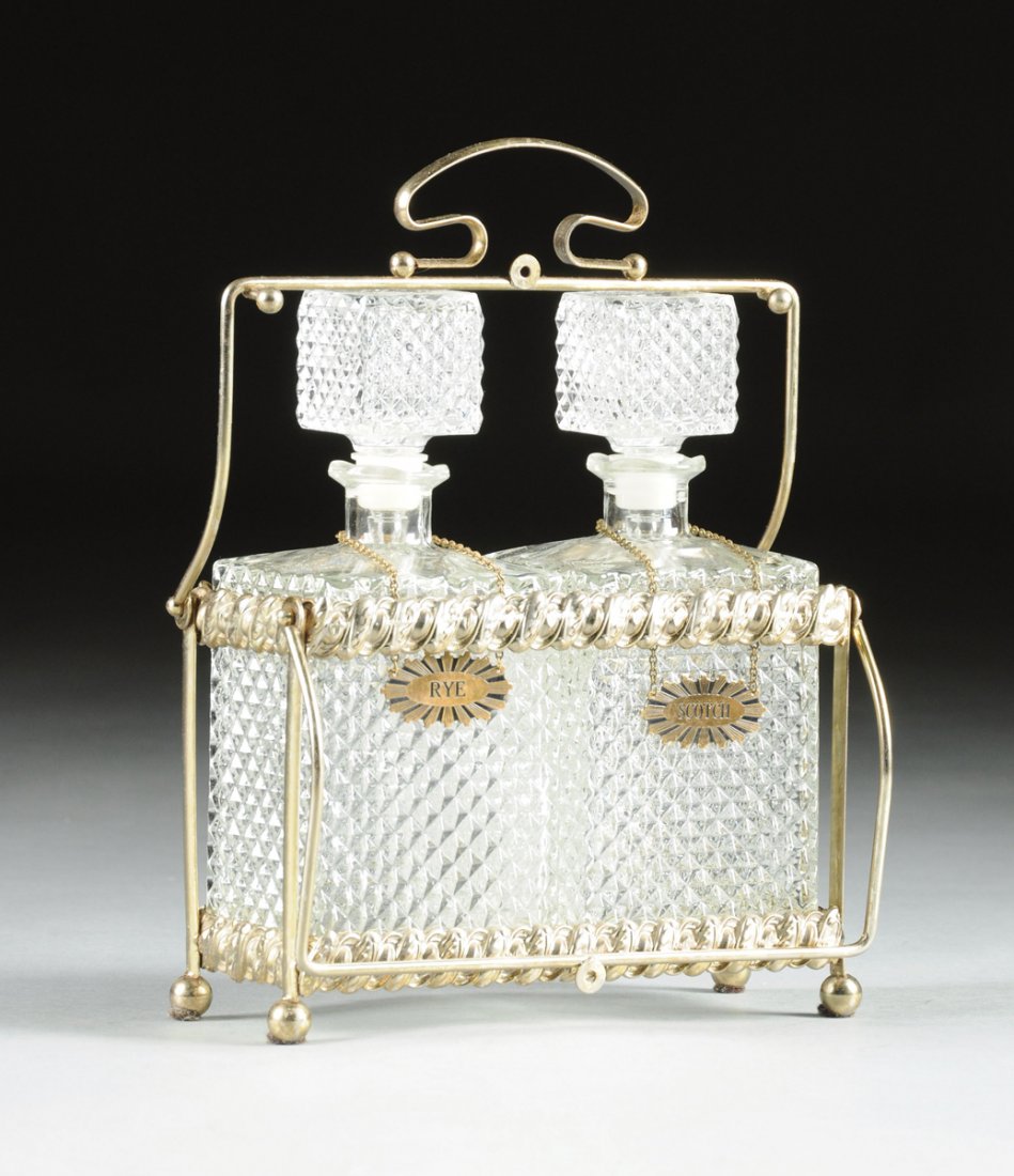 AN AMERICAN GLASS AND SILVER PLATE TWO BOTTLE LIQUOR: AN AMERICAN GLASS AND SILVER PLATE TWO BOTTLE LIQUOR TANTALUS, EARLY 20TH CENTURY, the silver plate frame of exposed rod construction with pressed rope form bands with alternating egg and leaf decorat