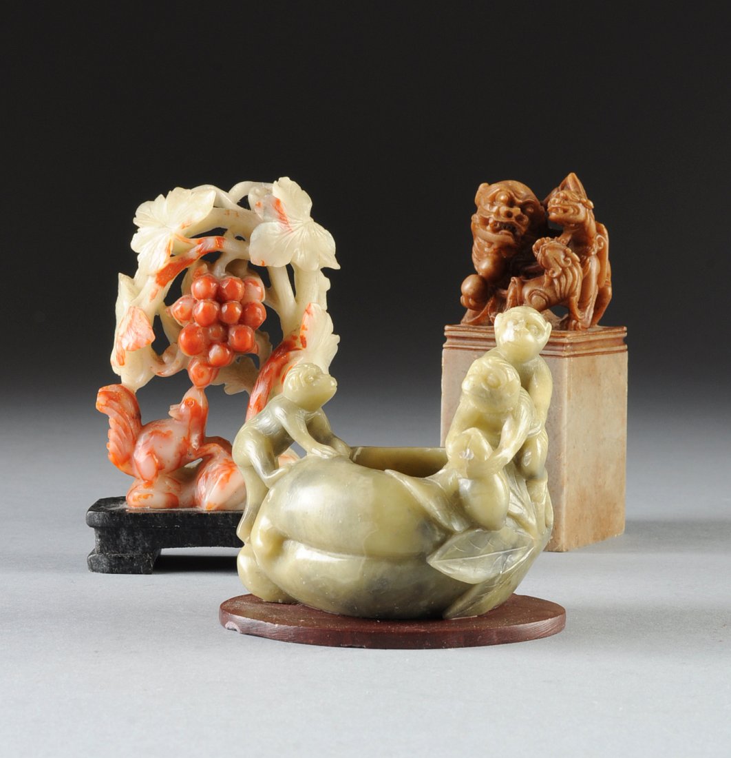 A GROUP OF THREE CHINESE CARVED SOAPSTONE FIGURAL: A GROUP OF THREE CHINESE CARVED SOAPSTONE FIGURAL GROUPS, 20TH CENTURY, comprising a brush pot of black veined pale green colors depicting three mischievous monkeys on a leafy gourd form pot with side