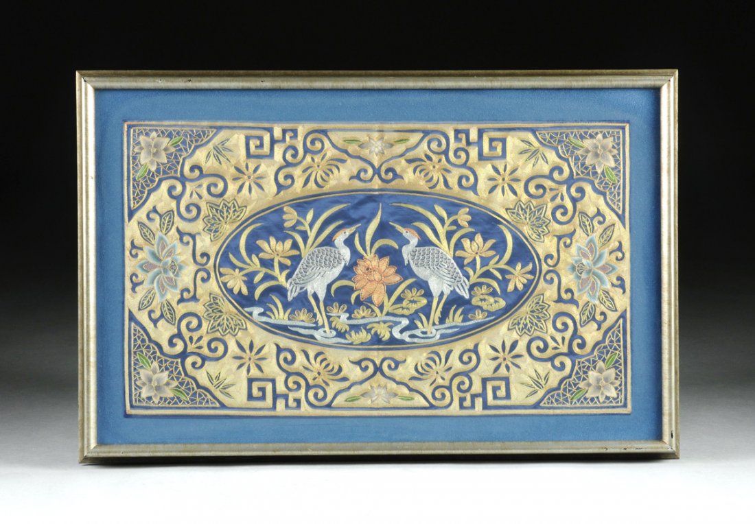 A FRAMED CHINESE SILVER AND GOLD METALLIC EMBROIDERED: A FRAMED CHINESE SILVER AND GOLD METALLIC EMBROIDERED SILK PANEL, 20TH CENTURY, the rectangular dark blue silk panel with center oval reserve depicting two addorsed cranes rendered in couched metallic