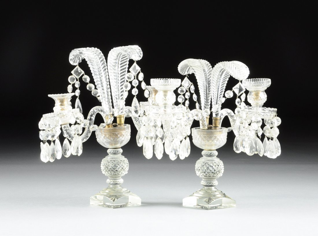 A PAIR OF GEORGE III STYLE CUT GLASS TWO-LIGHT: A PAIR OF GEORGE III STYLE CUT GLASS TWO-LIGHT CANDELABRAS, ANGLO-IRISH, each with a spherical diamond patterned stem supporting a similarly cut cup issuing Prince of Wales style feathers, flanked by 