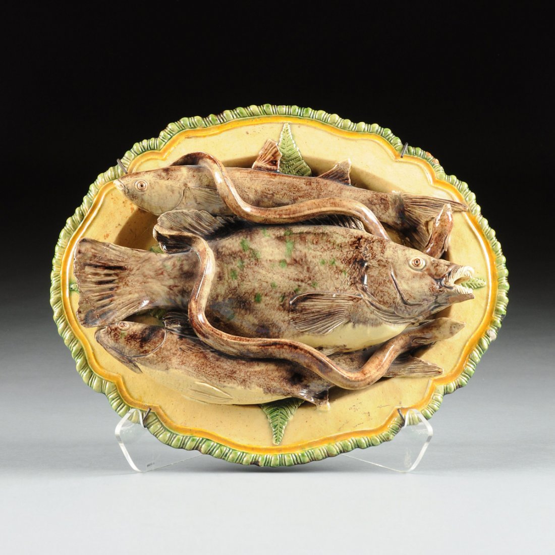 A MAFRA PALLISY WARE MAJOLICA CHARGER, CALDAS,: A MAFRA PALLISY WARE MAJOLICA CHARGER, CALDAS, PORTUGAL, CIRCA 1900, the oval mustard ground charger with shaped and gadrooned rim, the center layered with three applied fish and two eels over fern fr