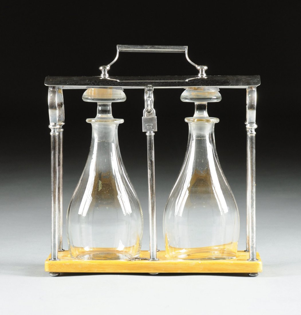 AN ENGLISH ART DECO CRYSTAL, BIRCH, AND CHROME TWO: AN ENGLISH ART DECO CRYSTAL, BIRCH, AND CHROME TWO BOTTLE LIQUOR TANTALUS, CIRCA 1935, the frame with six chrome columns supporting convex rotating lock bar with handle, birch base with cutouts for tw