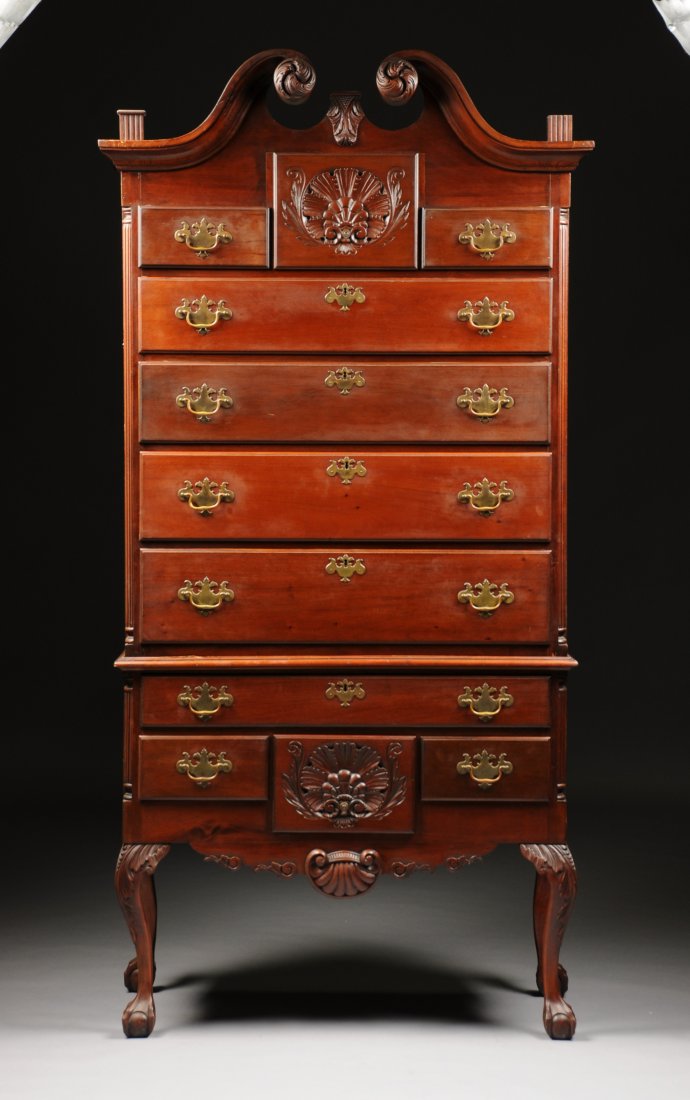 AN AMERICAN CHIPPENDALE STYLE CARVED MAHOGANY HIGHBOY,: AN AMERICAN CHIPPENDALE STYLE CARVED MAHOGANY HIGHBOY, the scrolled broken arched pediment separated by three urn form flaming finials, above a central shell carved drawer, flanked by two short drawer