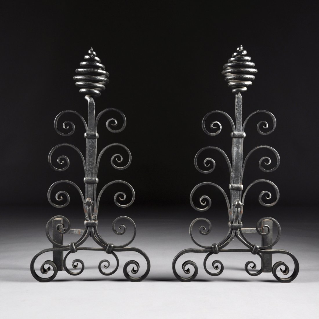 A PAIR OF CONTINENTAL WROUGHT-IRON CHENETS, POSSIBLY: A PAIR OF CONTINENTAL WROUGHT-IRON CHENETS, POSSIBLY FRENCH, LATE 19TH CENTURY, each having rows of graduated paired scrolls on a similarly detailed base and surmounted by a pear form coiled rod finia