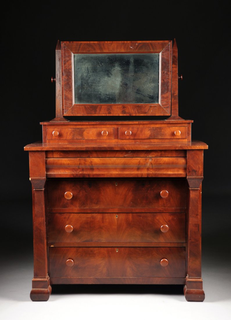 AN AMERICAN EMPIRE FLAME MAHOGANY DRESSER, 19TH: AN AMERICAN EMPIRE FLAME MAHOGANY DRESSER, 19TH CENTURY, the framed swivel mirror supported by obelisks on two inset short drawers, flanked by rectangular columns, on cushion molded square feet. Heigh