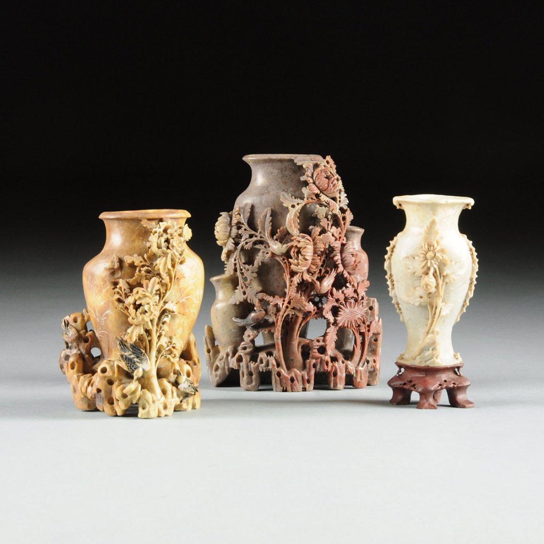 A GROUP OF THREE CHINESE CARVED SOAPSTONE VASES, 20TH: A GROUP OF THREE CHINESE CARVED SOAPSTONE VASES, 20TH CENTURY, one detailed in a red skinned neutral ground stone and modeled in reticulated deep relief as birds foraging amongst blossoming chrysanthe