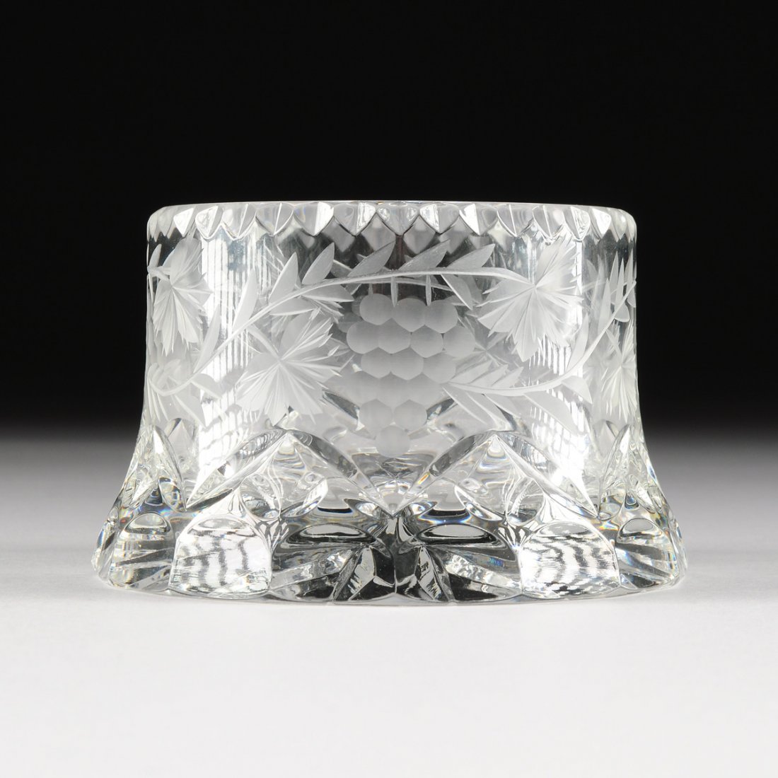 A CONTINENTAL CUT AND ENGRAVED CRYSTAL WINE COASTER,: A CONTINENTAL CUT AND ENGRAVED CRYSTAL WINE COASTER, MODERN, of flaring circular form and a scalloped rim above sides centering grapevine and cluster decoration over a scalloped base rim, enclosing a