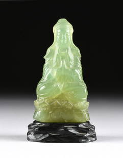 A CHINESE CARVED TRANSLUCENT GREEN HARDSTONE FIGURE OF: A CHINESE CARVED TRANSLUCENT GREEN HARDSTONE FIGURE OF BUDDHA, MODERN, modeled in a seated position with legs crossed and a smiling serene expression, above hands in prayer mudra while wearing