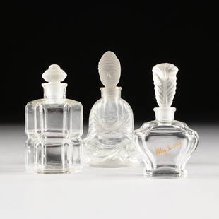 A GROUP OF THREE FROSTED AND CLEAR MOLDED GLASS PERFUME: A GROUP OF THREE FROSTED AND CLEAR MOLDED GLASS PERFUME BOTTLES, 20TH CENTURY, one modeled as a seated Buddha with a frosted stopper detailed in a tightly curled hairstyle above a serene expression, o