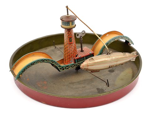 An unusual clockwork tinplate airship toy. Produced by: An unusual clockwork tinplate airship toy. Produced by CKO (Kellerman) in the 1920’s. A 20cm tinplate dished tray, 2cm deep probably to contain water. Over which is a double arched bridge with a lig
