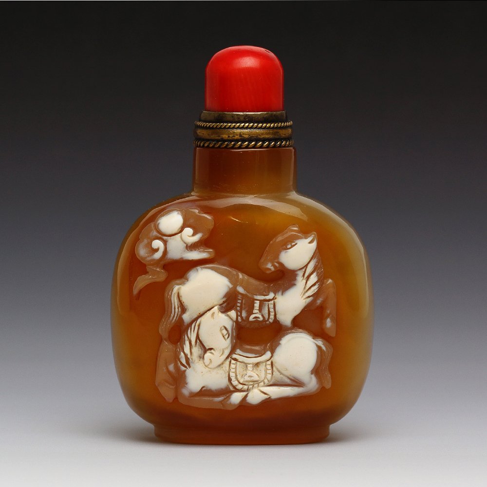 CHINESE CAMEO CARVED AGATE SNUFF BOTTLE: Chinese finely hollowed, cameo carved agate snuff bottle; of flattened circular form; the front with design of two horses and a cloud above in relief, ; good use of color; red coral stopper; H: 3.2’