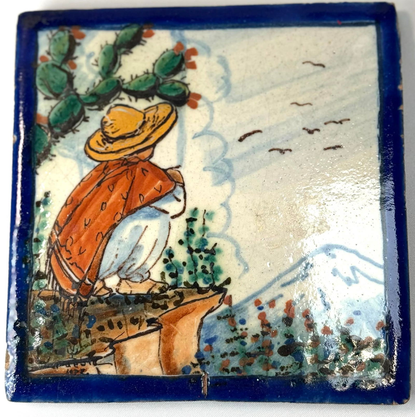 Vintage Hand-Painted Talavera Tile – Mexican Folk Art, C. 1940s–1960s: Charming vintage Mexican Talavera ceramic tile featuring a hand-painted folk art scene of a campesino in a hat and poncho overlooking a mountain landscape with cactus. Vibrant colors and classic cobal