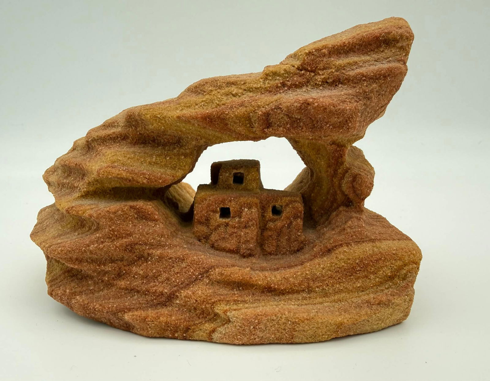David Jeffery Hand-Carved Sandstone Sculpture – Cave Dwelling Form, Signed: Hand-carved sandstone sculpture by David Jeffery, depicting a stylized architectural cave-dwelling form carved directly from a single block of layered sandstone. The composition features a natural arc