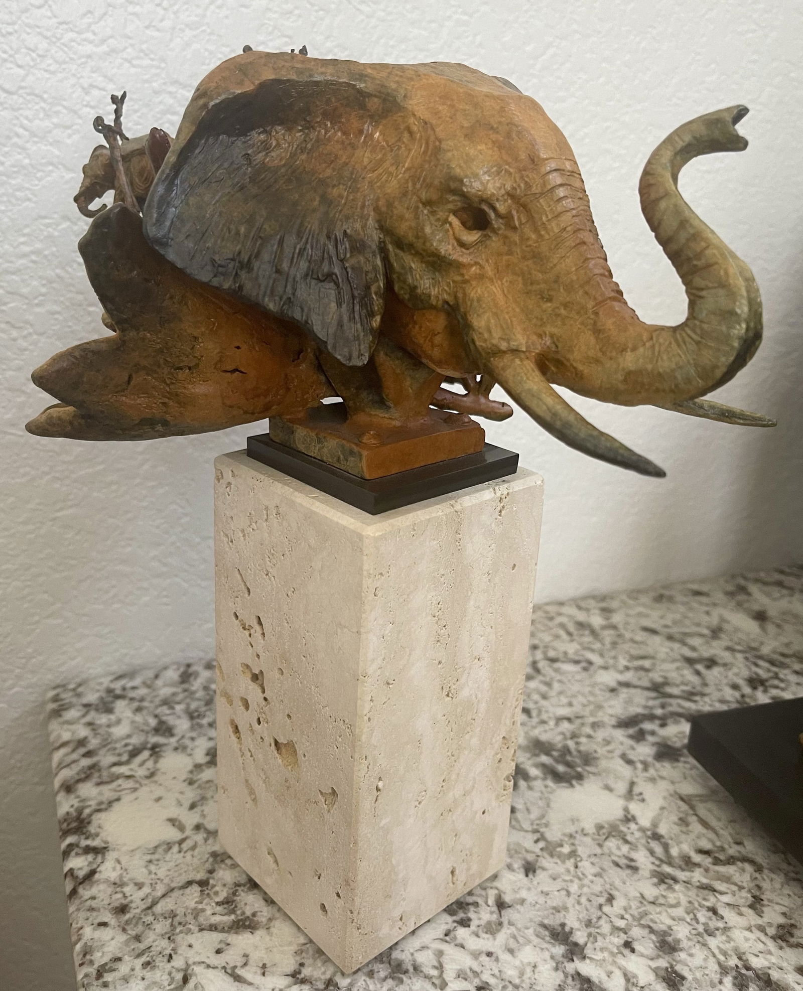 Theodore “Ted” Gall Bronze Elephant Head Sculpture on Travertine Base: Striking bronze elephant head sculpture by Theodore Ted Gall, executed in rich mixed brown and green patinas and presented on a substantial travertine stone base with black marble plinth. The sculptur