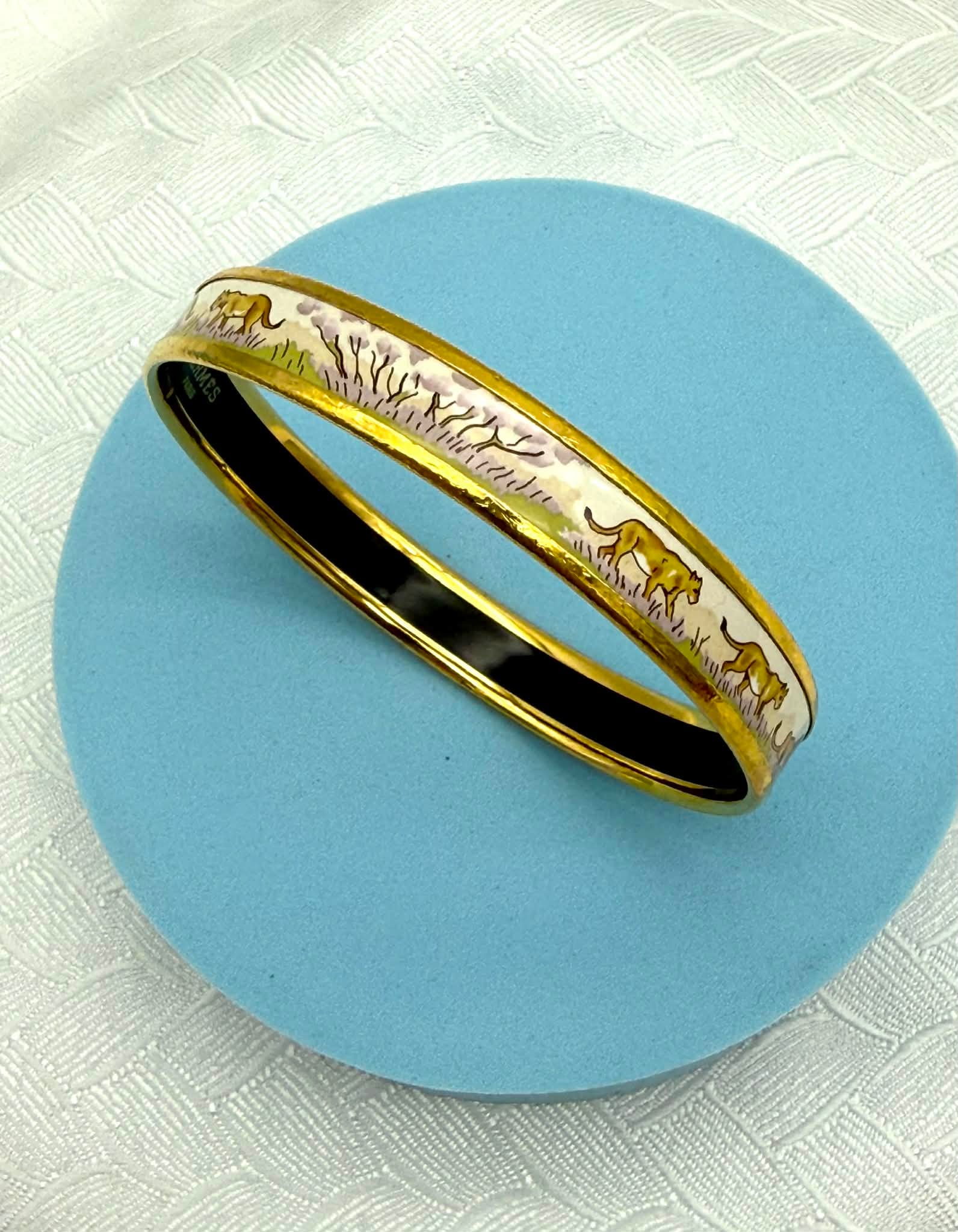 Hermès Paris Enamel Lion Safari Bangle Bracelet w/ Box & Certificate – Made in Austria: Elegant Hermès Paris enamel bangle bracelet featuring a finely detailed safari lion motif set against a soft ivory ground. The design depicts lions walking and resting among stylized grass and landsc