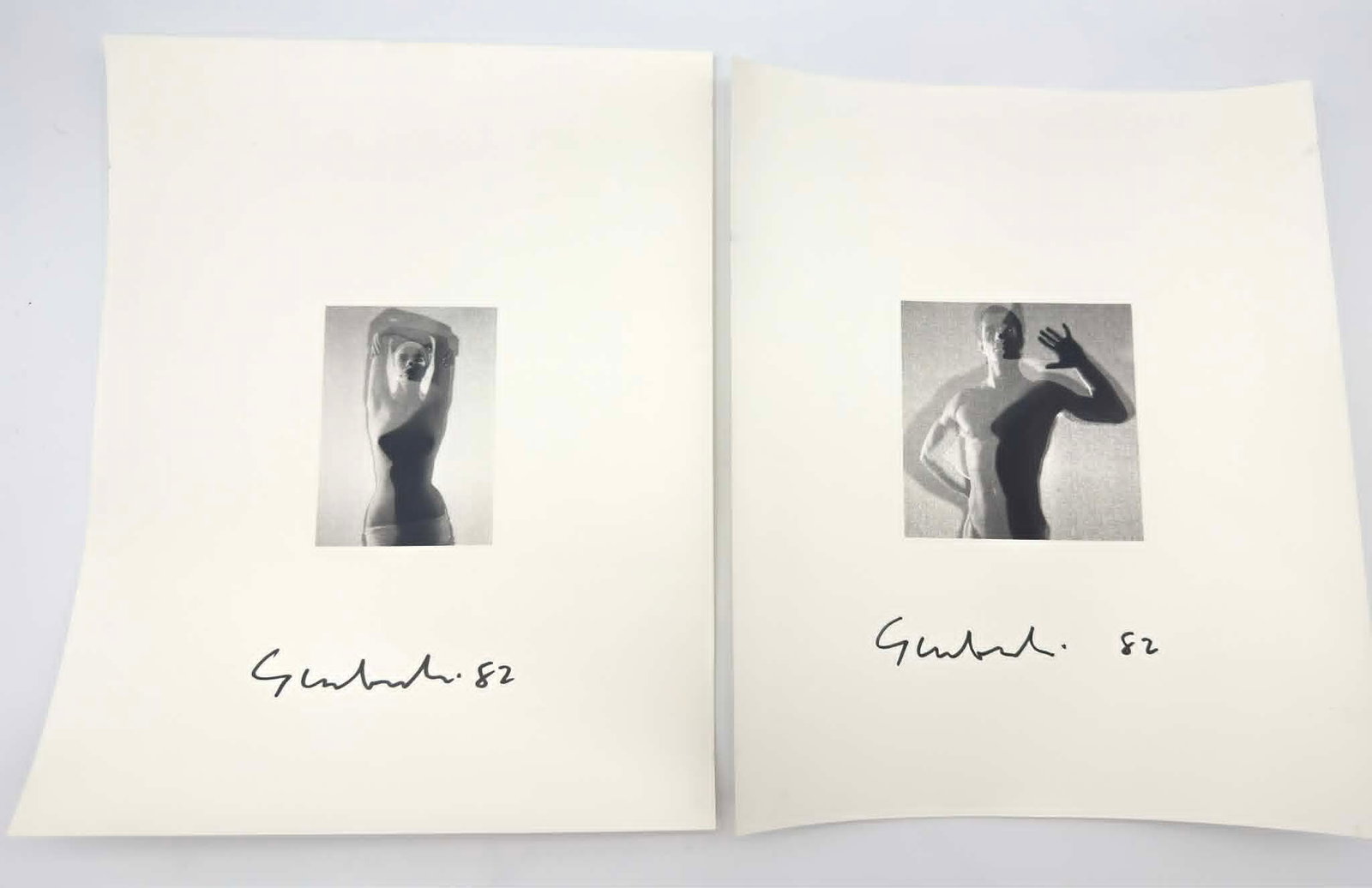 Pair of Signed Gelatin Silver Photographs, Nude Studies Behind Scrim, 1982: Group of two gelatin silver photographs depicting stylized nude figure studies photographed behind a translucent scrim, creating a soft-focus interplay of light and shadow. The compositions emphasize 