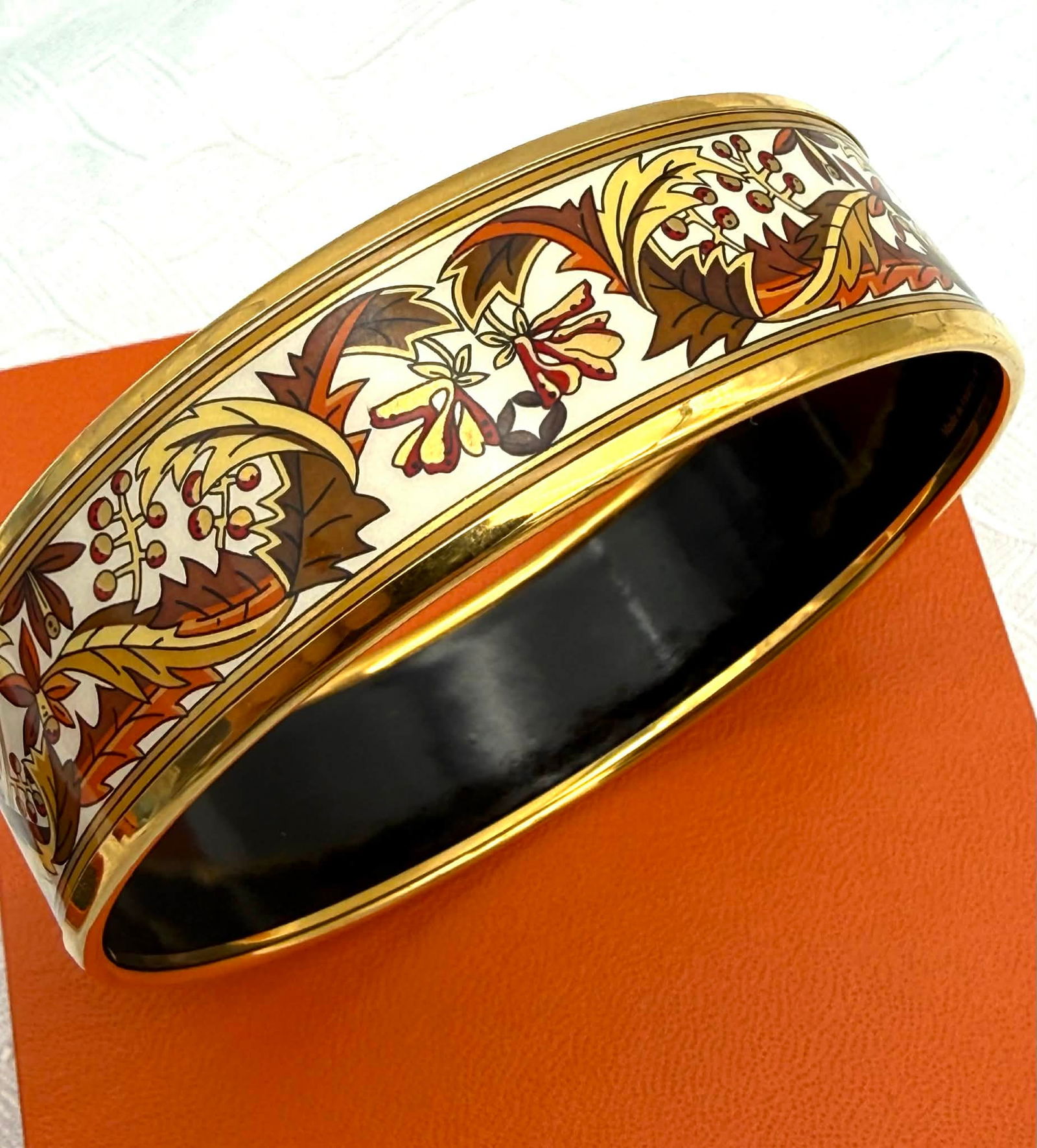 Hermès Paris Wide Enamel Bangle Bracelet – Autumn Floral Motif – Austria – With Box: Striking Hermès wide enamel bangle bracelet featuring an elegant autumnal floral motif rendered in warm earth tones including cream, ochre, rust, brown, and soft gold. The continuous botanical design