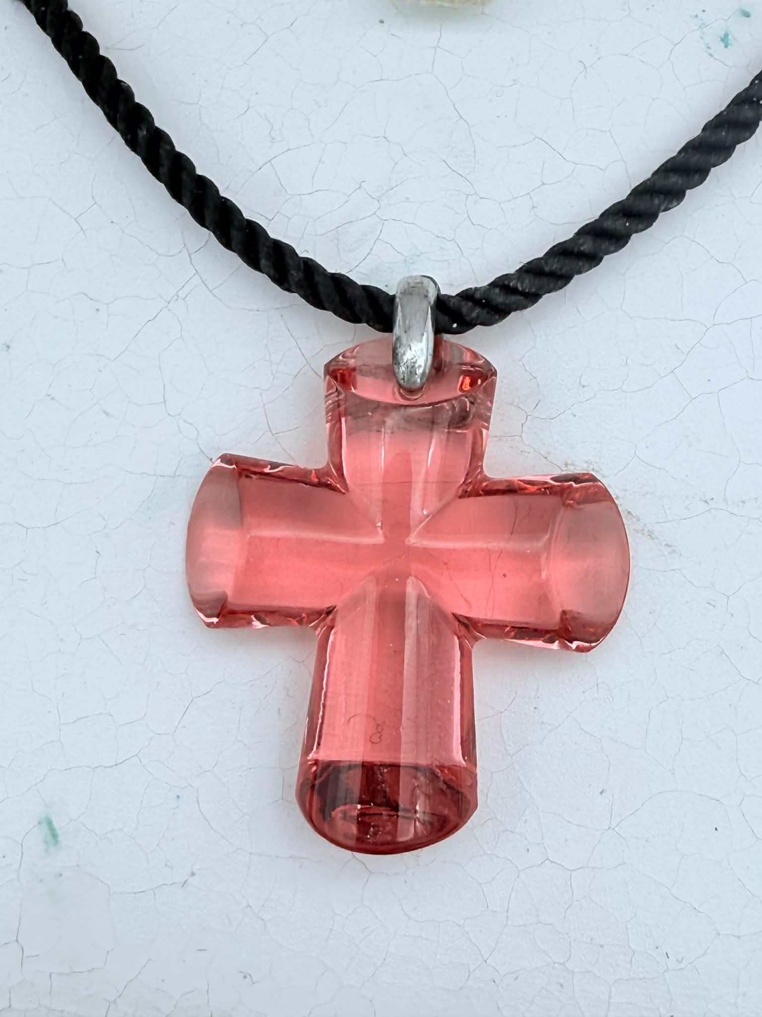 Baccarat Light Red Crystal Cross Pendant Necklace – France – With Box: Authentic Baccarat crystal cross pendant necklace featuring a faceted translucent red crystal cross with strong clarity and light refraction. The sculptural pendant is suspended from a black cord neck