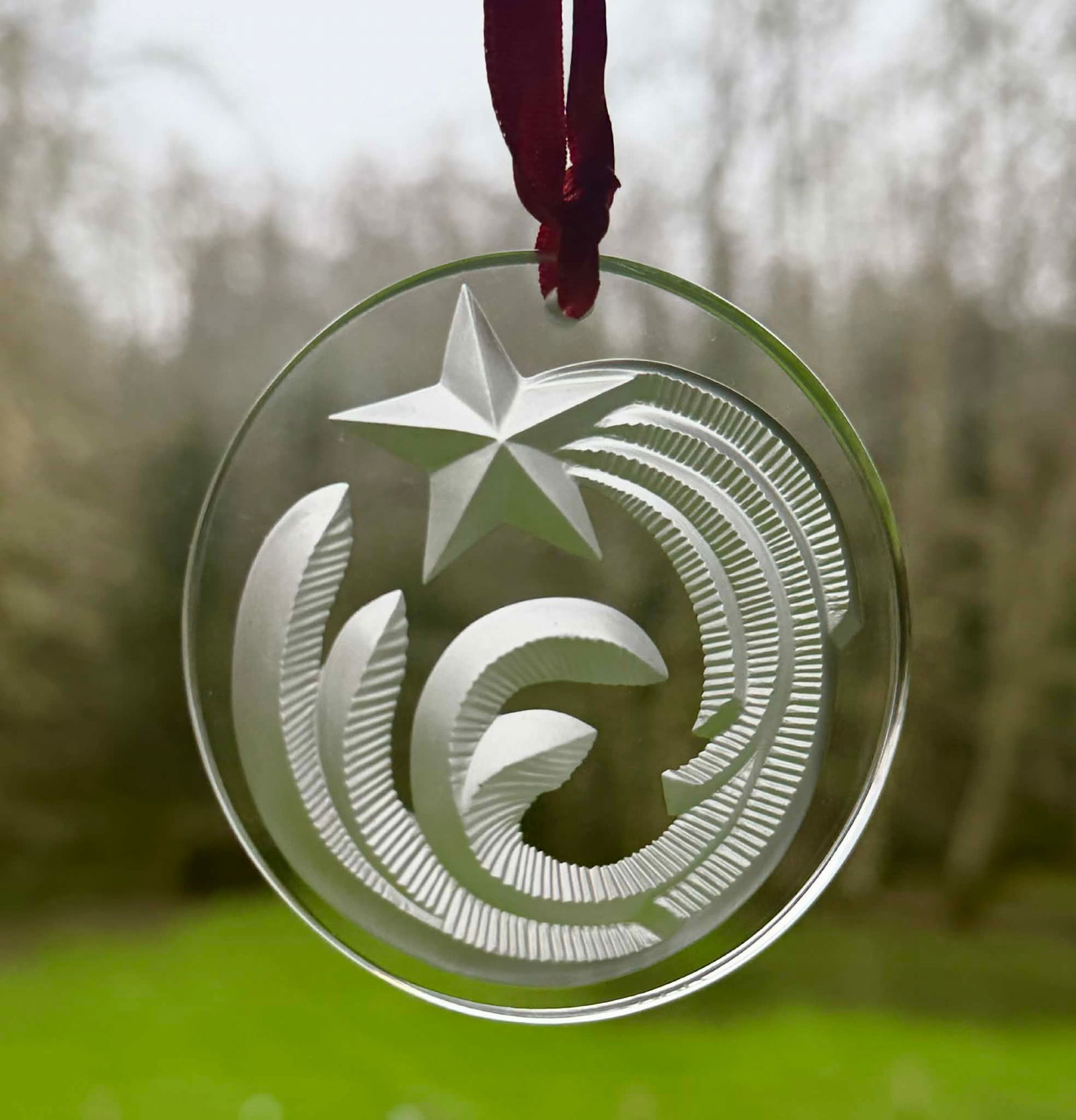 Lalique Crystal “Noël 2000” Christmas Ornament: Signed crystal Christmas ornament produced by Lalique, engraved along the edge “Noël 2016.” The circular clear crystal ornament features a stylized star with sweeping comet-like forms rendere