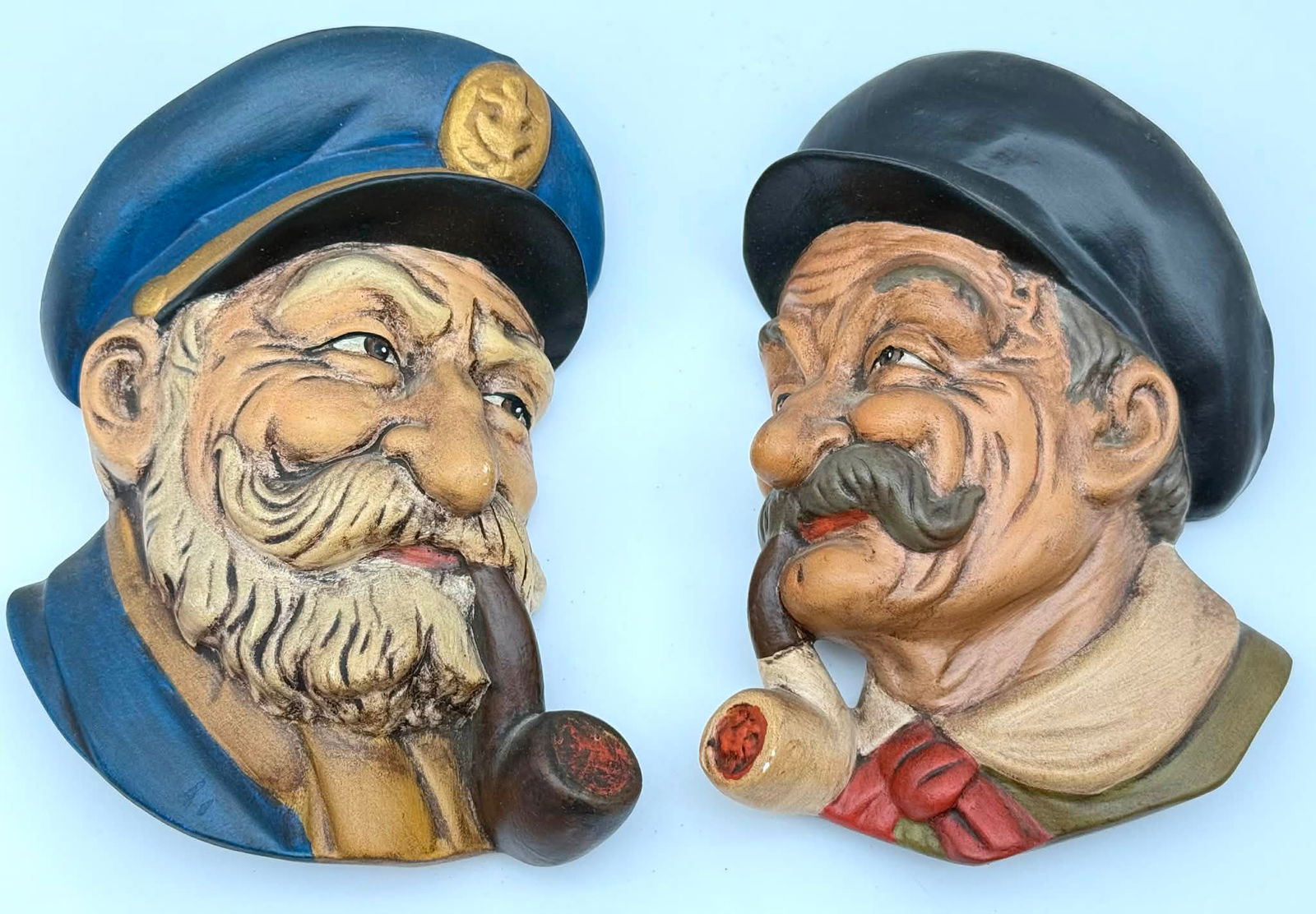 Pair Vintage Carved Figural Wall Plaques Smoking Gentleman Heads Hand Painted: Pair of vintage carved figural wall plaques depicting expressive male character heads, each shown with a pipe motif. One figure features a bearded man wearing a blue cap, while the other depicts a mus