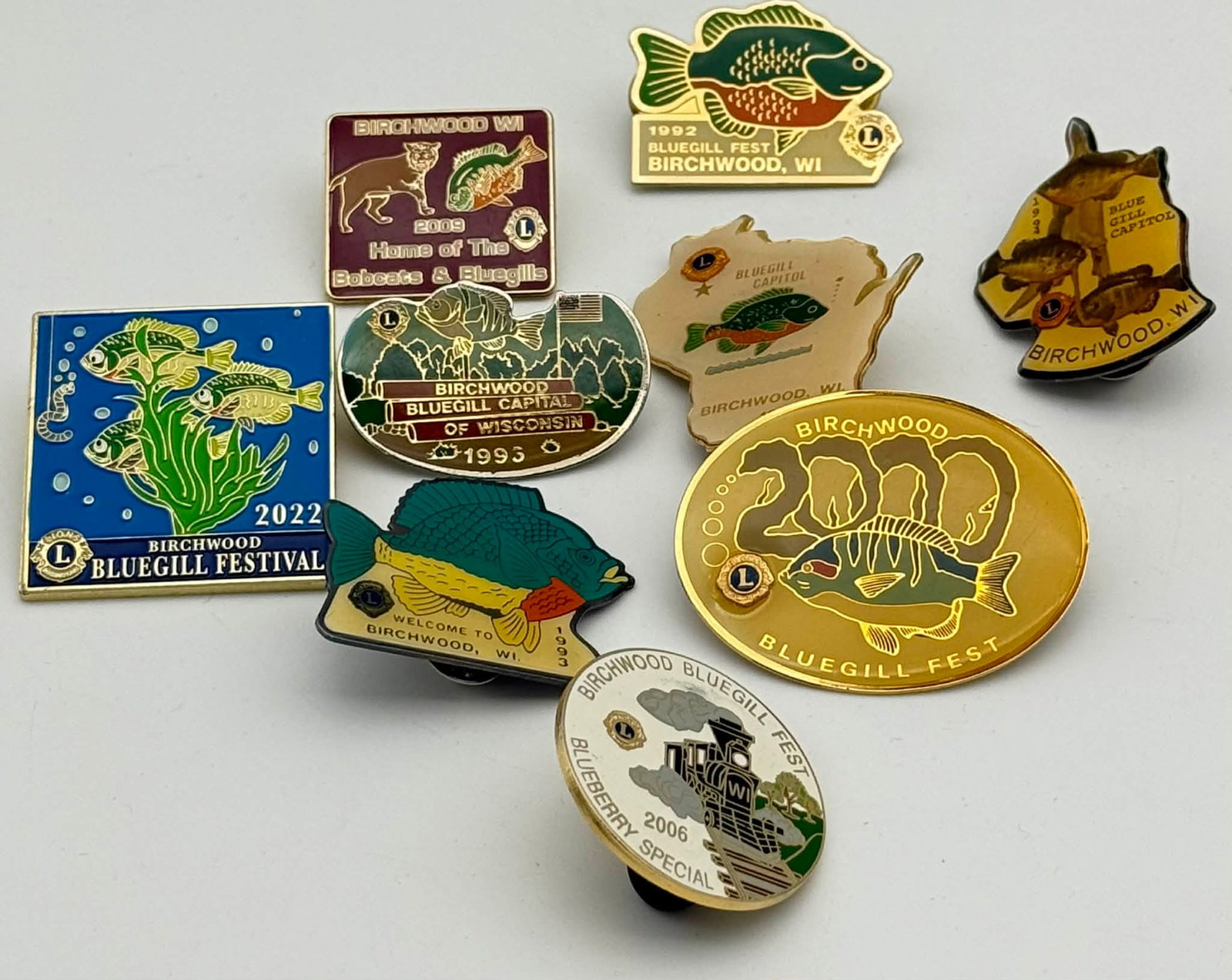 Lot of Birchwood WI Bluegill Festival Pins Lions Club 1992–2022 Enamel Badges: Collection of enamel souvenir and commemorative pins from Birchwood, Wisconsin, celebrating the annual Bluegill Festival and local Lions Club events. The group includes multiple examples spanning diff