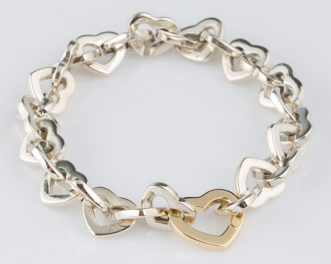 TIFFANY & CO STERLING SILVER &14K HEART BRACELET: TIFFANY & CO STERLING SILVER &14K HEART BRACELET 7.5 in sterling silver linking hearts with 1 larger 14k yellow gold heart in center of bracelet. Produced by renowned designer Tiffany & Co. Weight: 34