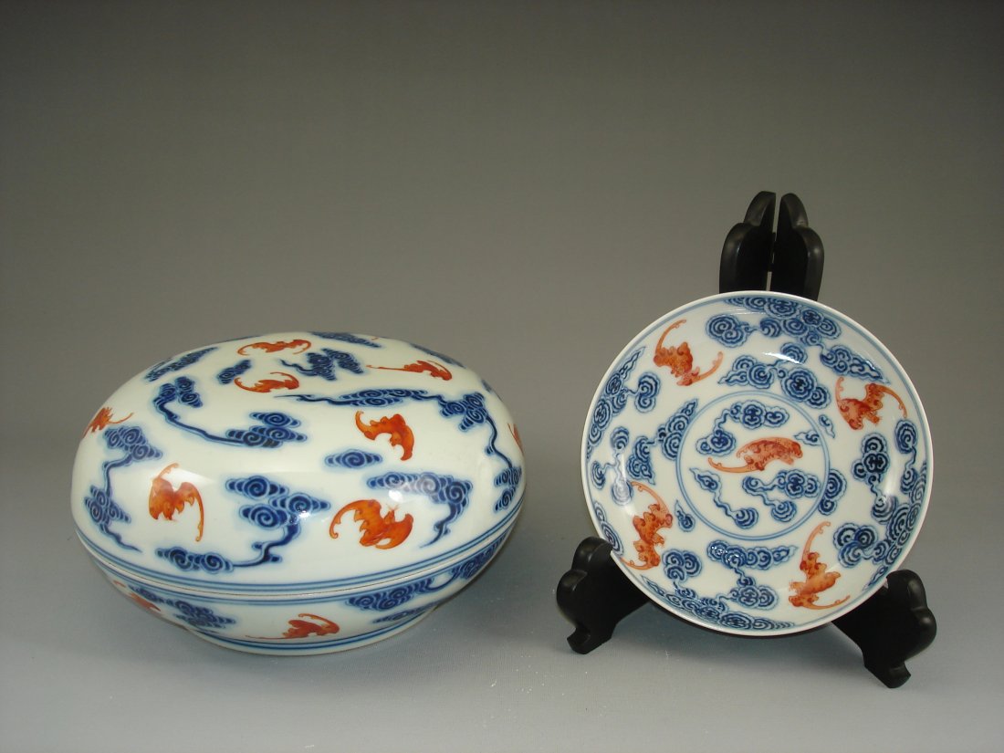 Underglazed red & blue round box and saucer: Guangxu period, underglazed red & blue box (4.5"H X 8.125"D) repaired at the cover and a saucer ( 5 3/4" D) , decorated with clouds and iron red bats. Wood stand is not including. Provenance: Lot # 19