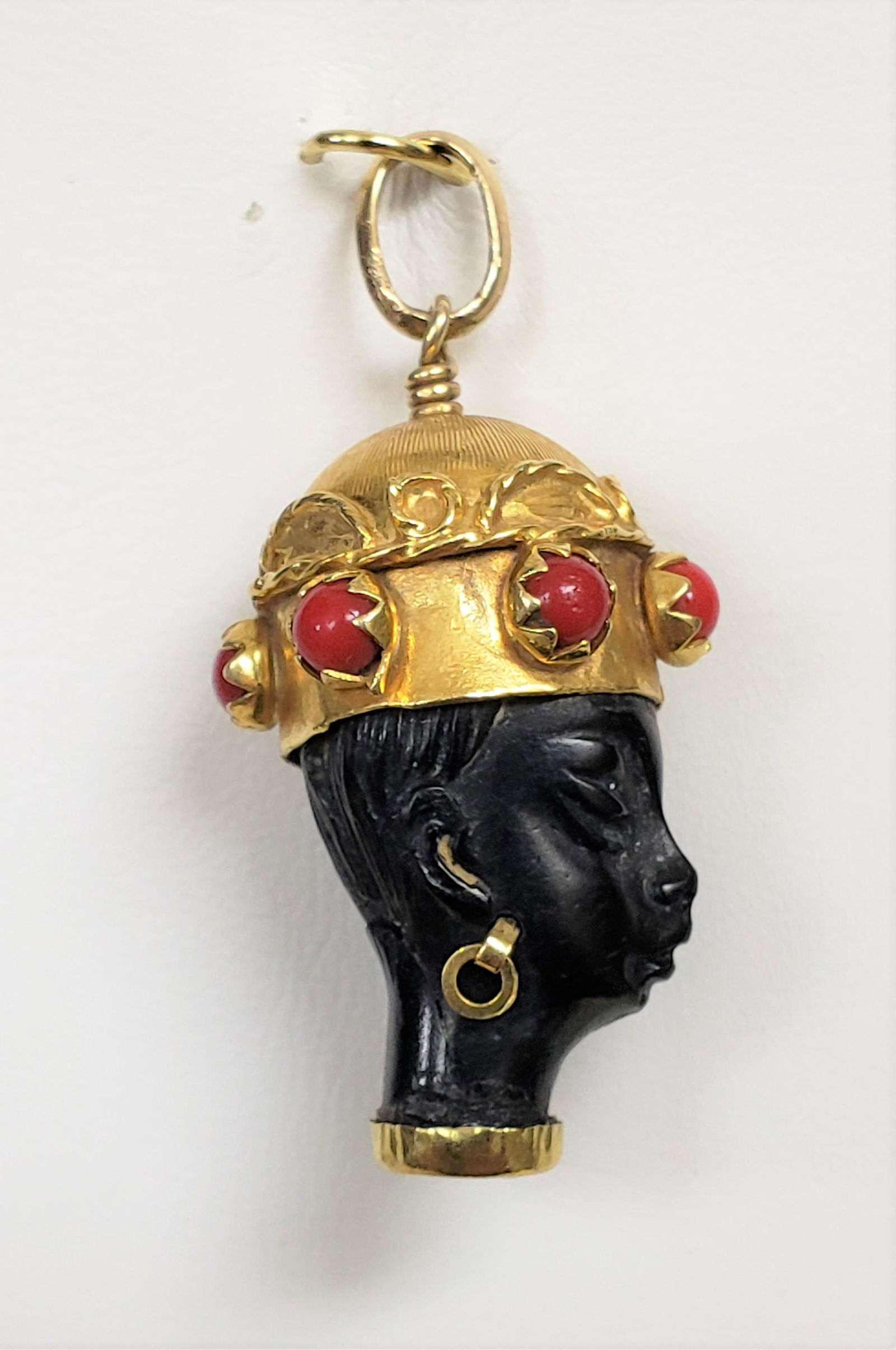 1960's 18K Blackamoor Pendant By Corletto: This is a 1960's 18k Blackamoor pendant by Corletto. The pendant features a hand carved ebony bust accented with applied 18K yellow gold highlights. It is studded with ox blood coral cabochons. It wei