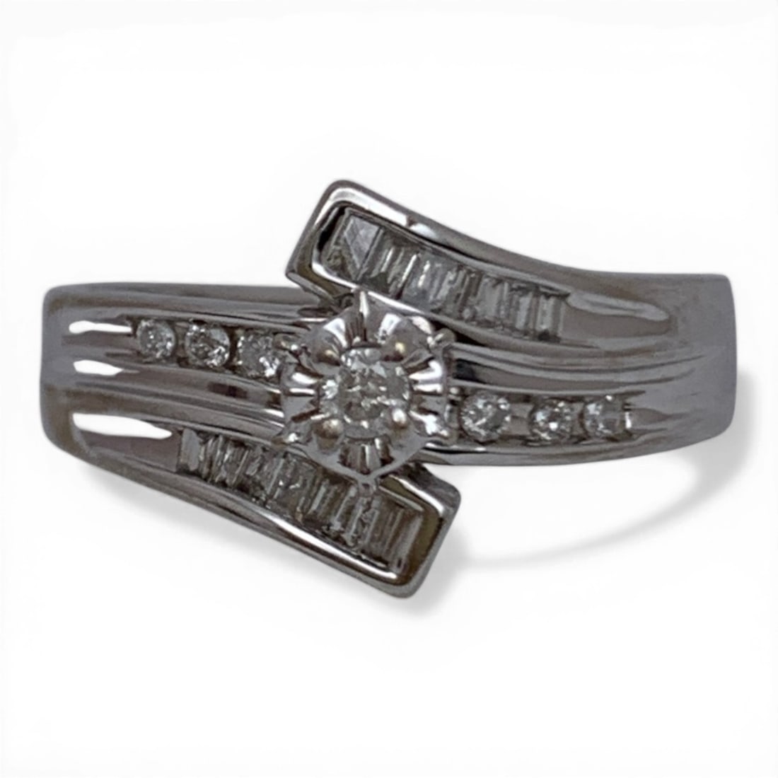 10k White Gold & Diamond Ring: 10k White Gold Ring With A Bypass Design Featuring 1 Round Cut Solitaire Raised Diamond Approx. 0.07ct Flanked By 6 Round Cut Diamonds Approx. 0.014ct Each & 14 Baguette Cut Diamonds Marked 10k -