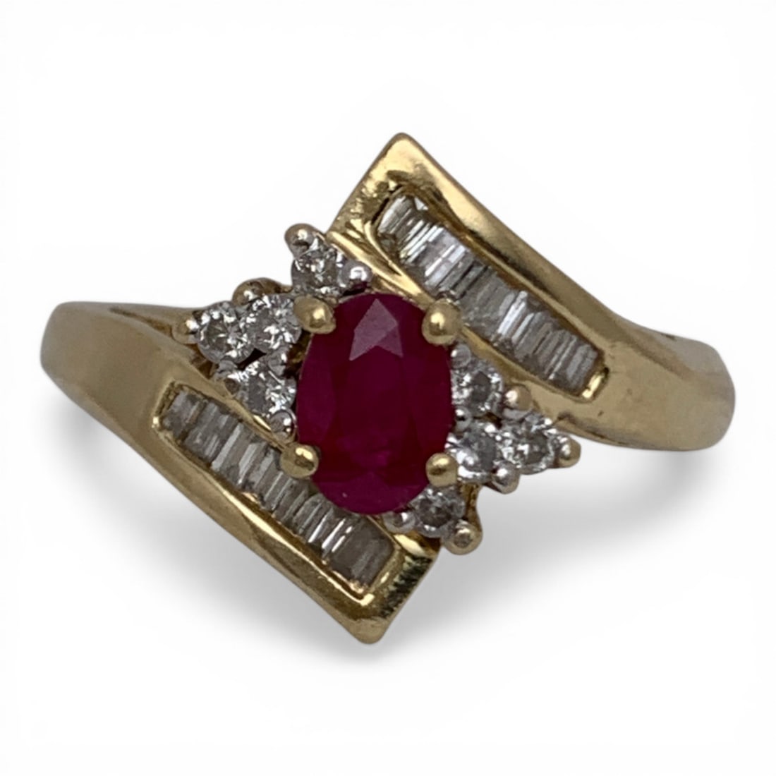 14k Gold Diamond & Ruby Bypass Design Ring: 14k Yellow Gold Diamond & Ruby Ring Featuring A Raised Central Oval Cut Ruby Approx. 0.50ct Flanked By 8 Round Cut Diamonds Approx. 0.03ct Each. The Band Is In A Bypass Design With 14 Baguette Cut