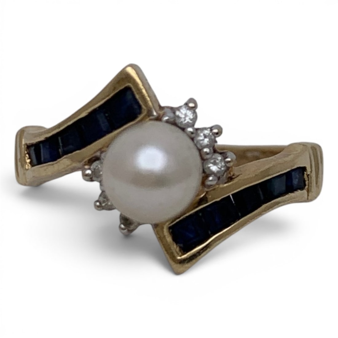 Vintage 14k Gold Diamond Pearl & Sapphire Ring: 14k Yellow Gold Ring With A Bypass Design Featuring A Center Set White Pearl Flanked By 6 Round Cut Diamonds. Channel Set Along The Band Are Square Cut Blue Sapphire GemstonesMarked 14k - Size 6.25 - 