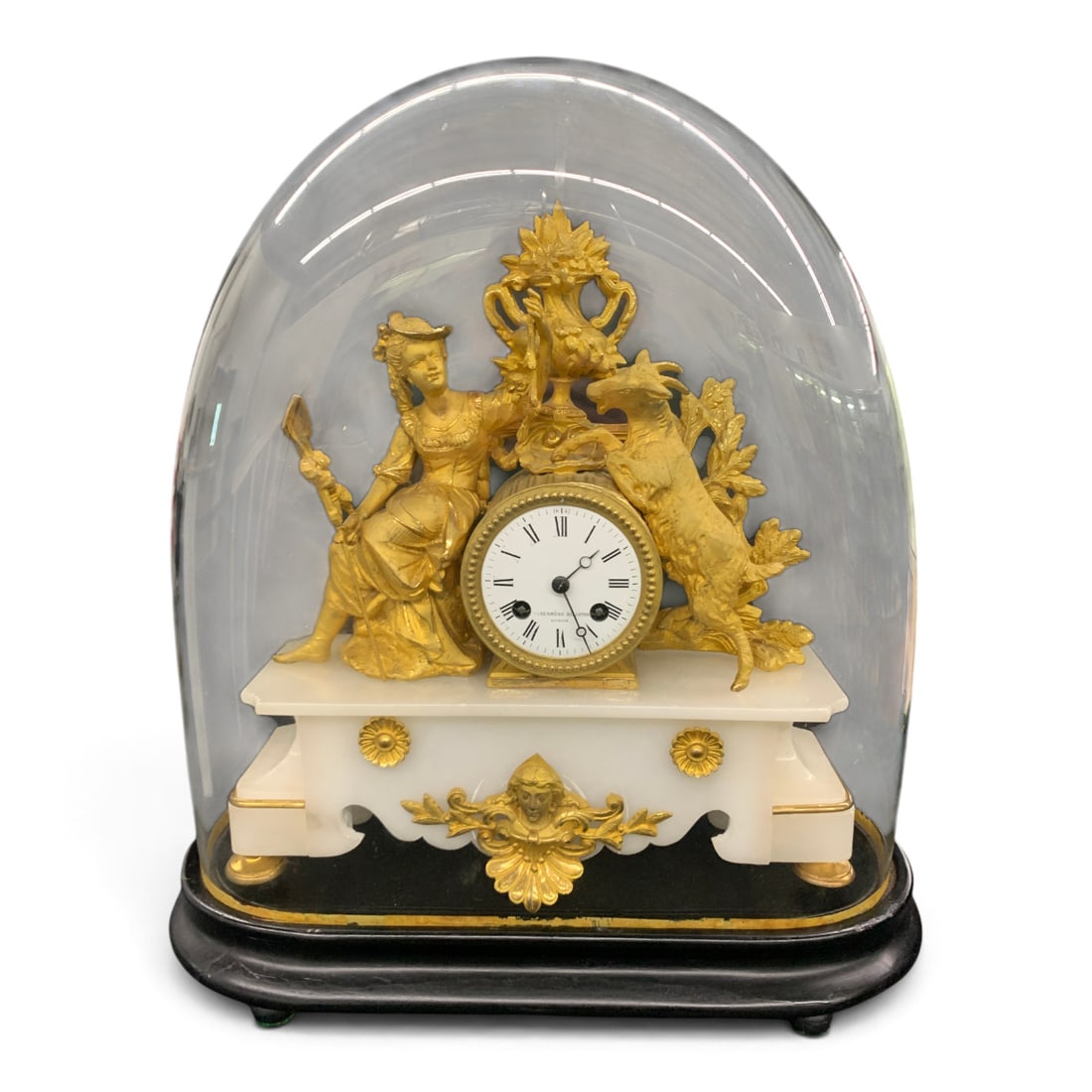 Antique German Mantel Clock: Antique German Mantel Clock Featuring A Gilt Metal Sculpture Above The Clock Movement Sat On A White Alabaster Base. The Mantel Clock Is Sat On A Wooden Black Oval Pinth With A Custom Glass
