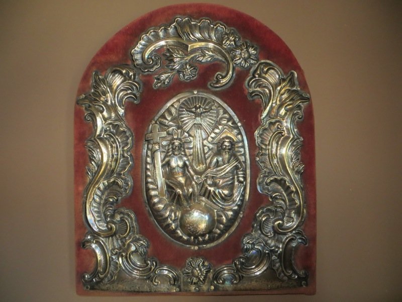 Spanish Colonial Silver Altar Decoration: A Spanish Colonial silver altar decoration from Central America, the red cloth covered domed panel applied with a central oval of the Holy Trinity surrounded by sprays of Rococo scrolls and foliage, i