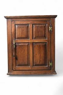 A George III oak panelled wall hanging cupboard: A George III oak panelled wall hanging cupboardOf rectangular outline, the ogee cornice above a single door with four fielded panels, opening to two fixed shelves, two small drawers flanked by two con