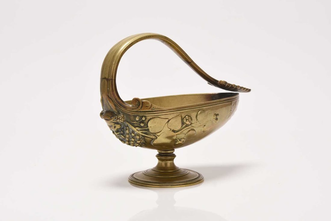 After Ferdinand Levillain (1837-1905), a neoclassical bronze vessel: After Ferdinand Levillain (1837-1905), a neoclassical bronze vesselOf footed boat form with scroll handle terminating in an anthemion form, the bowl moulded with a mask issuing fruiting vines.16cm acr