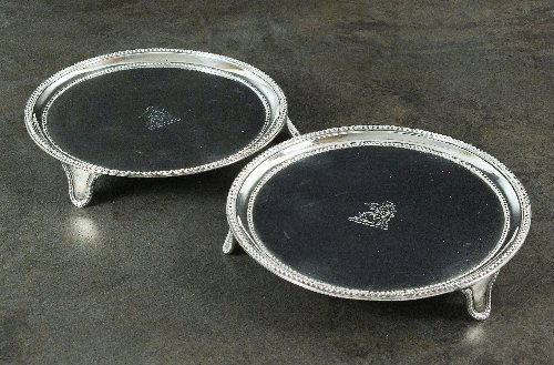A pair of George III silver card salvers, Robert: A pair of George III silver card salvers, Robert Hennell I, London 1792, each with engraved crest to centre, beaded rim and raised on three bracket feet with conforming bead decoration, 15.5cm diamete