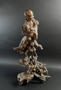 A Chinese root wood carving of a mighty guard Luohan,: A Chinese root wood carving of a mighty guard Luohan, 19th century, naturalistically detailed, looking fierce, his arms holding s staff, standing on a base, staff missing, 75cm high overall. Note:'The