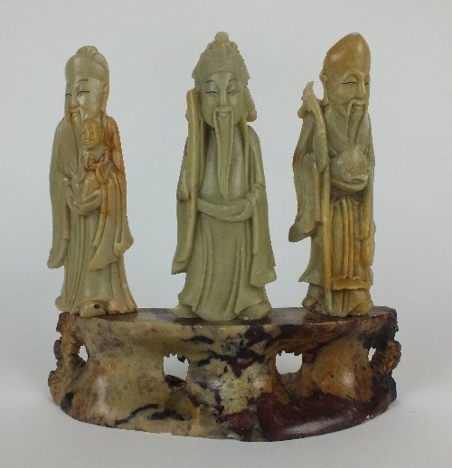 A Chinese carved soapstone group of the three gods of: A Chinese carved soapstone group of the three gods of good fortune; Fu, Lu, and Shou, early 20th century, each carved holding their traditional attribute on a pierced oval plinth, 17cm high, 18cm wide