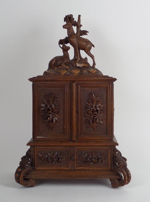 An early 20th century Black Forest walnut table: An early 20th century Black Forest walnut table cabinet, the deer carved pediment over two cabinet doors each with florally moulded single panel, opening to reveal four shallow drawers fitted with kno
