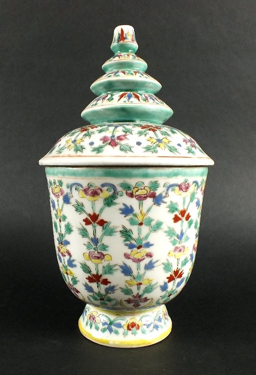 An Indonesian market jar and cover, 20th century, the: An Indonesian market jar and cover, 20th century, the cover of distinctive tiered pagoda form, decorated with a floral pattern in greens, reds, yellows pinks and blues, 20.5cm high (at fault)