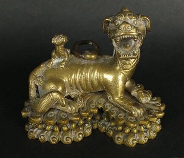 A Chinese brass scroll weight, 20th century, modelled: A Chinese brass scroll weight, 20th century, modelled as a female Fu dog lying on a lotus style throne, her head raised and mouth open as if roaring, her cub looking towards her as it climbs on her