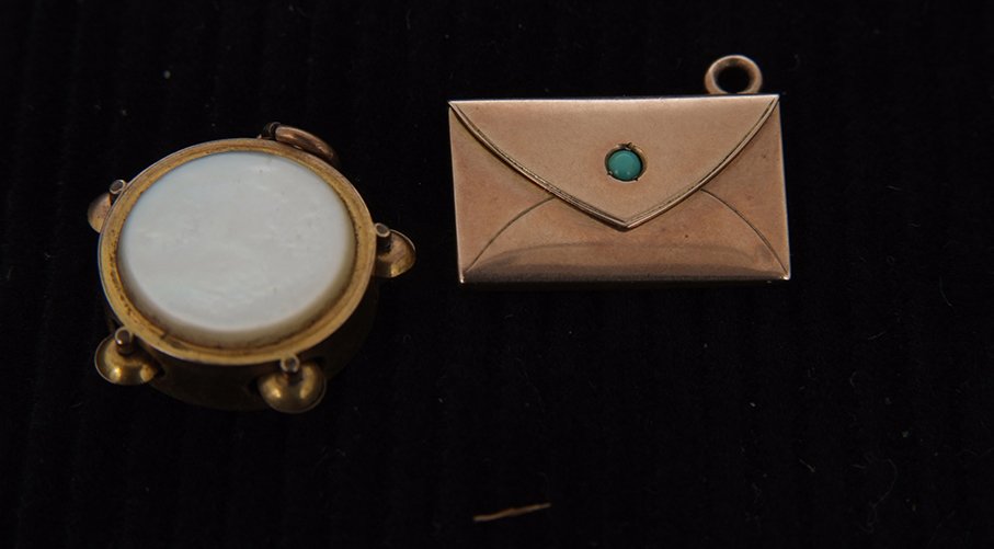 Two Edwardian gold charms, an envelope set with a: Two Edwardian gold charms, an envelope set with a turquoise, and a tambourine with mother of pearl drum skin, both unmarked. (2)