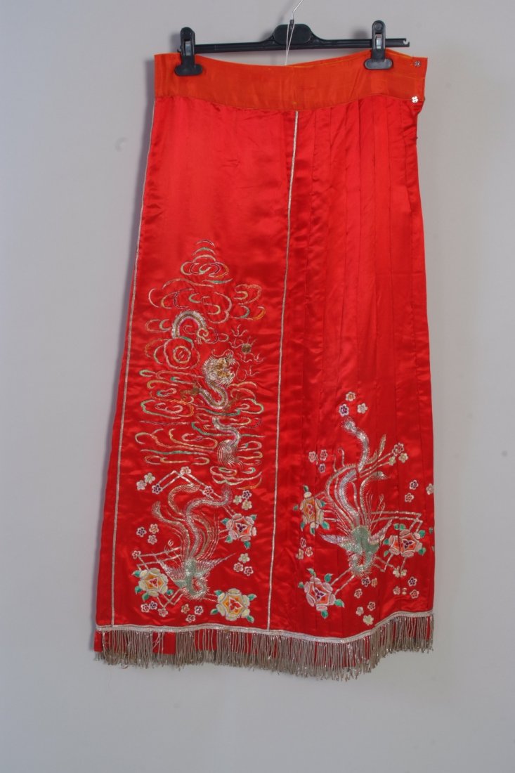 An Antique Chinese Red Noble Wedding Skirt. The skirt: An Antique Chinese Red Noble Wedding Skirt. The skirt is made from fine soft red satin silk. The gold crewel work depicts a dragon with four claws above a bird of paradise. The hem of the skirt has go