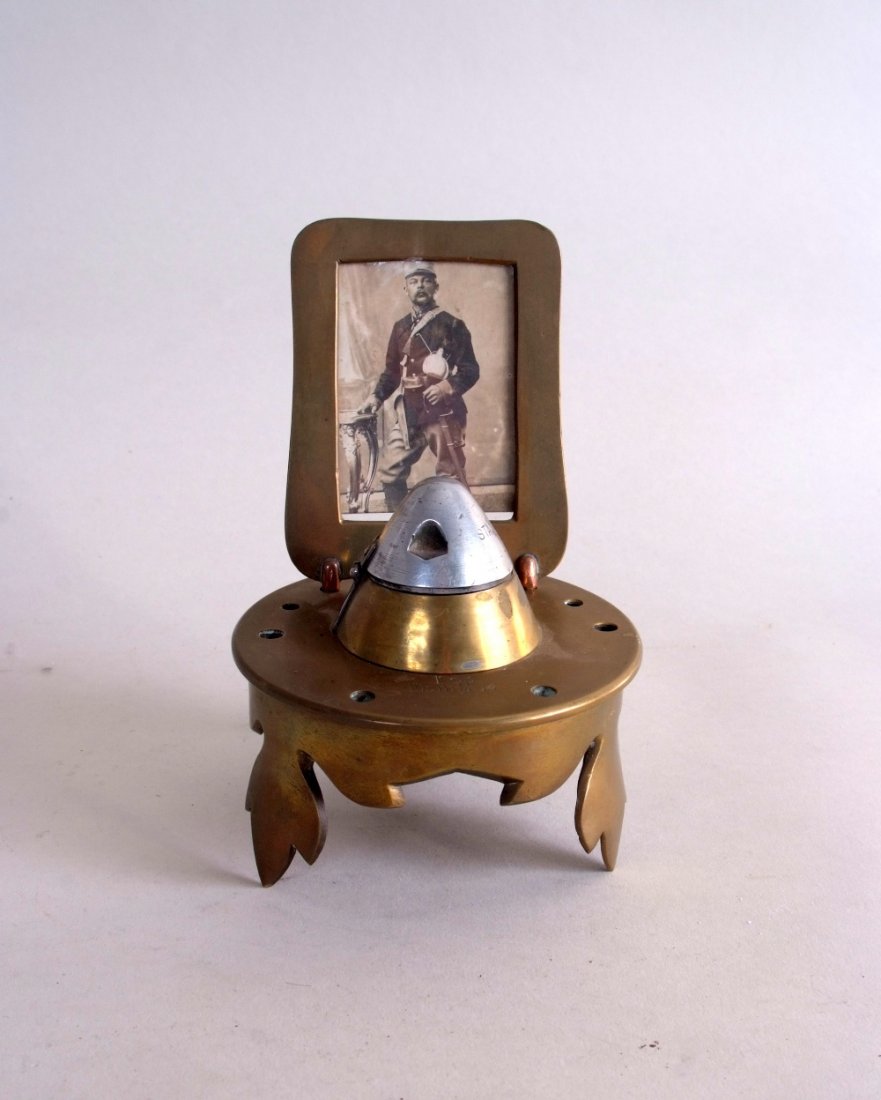 WWI trench art - A brass shell casing moulded into a: WWI trench art - A brass shell casing moulded into a lamp with leaf carved legs, bearing a glazed photograph of an Austro-Hungarian officer, the lamp centred with a hinged lid, stamped 1917 and variou