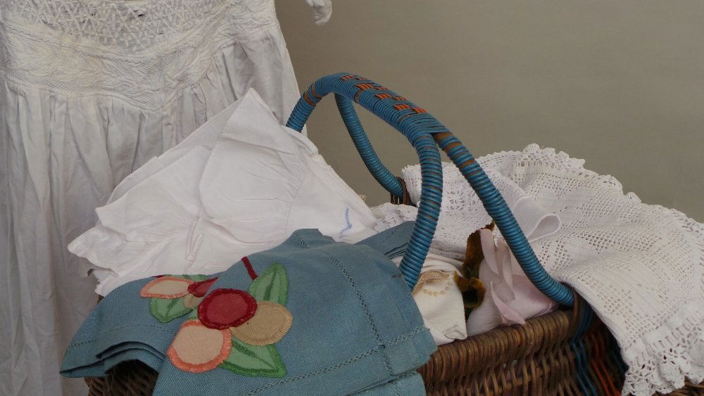 Good lot of linens and tablewear. A vintage cotton: Good lot of linens and tablewear. A vintage cotton nightgown and one other. Laundry tongs and early plastic glove savers - all in a 1950's basket