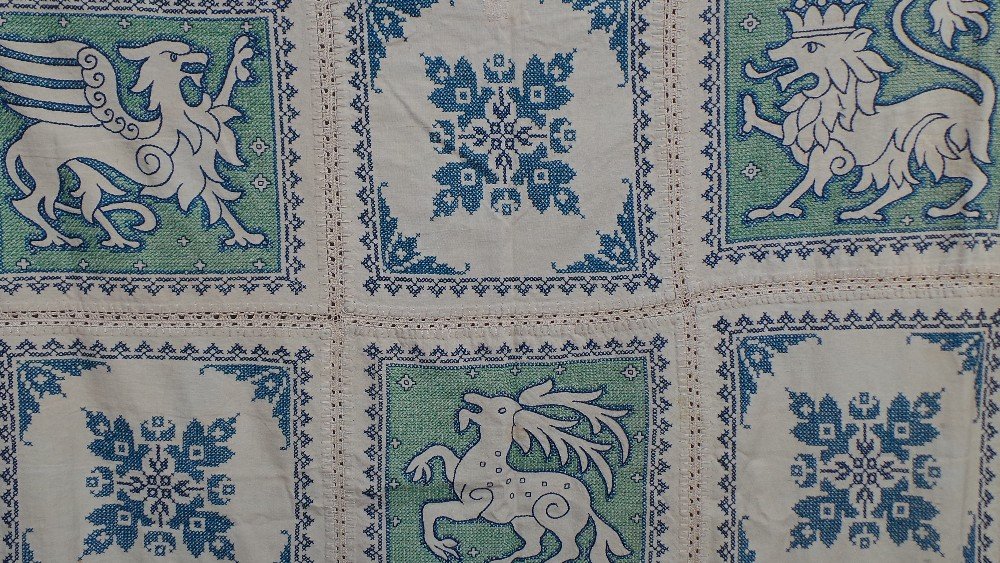A beautiful folk art linen throw made up from: A beautiful folk art linen throw made up from individual embroidered squares depicting gryphons and other mythical beasts. The embroidery has been executed in both cross and straight stitch. There are