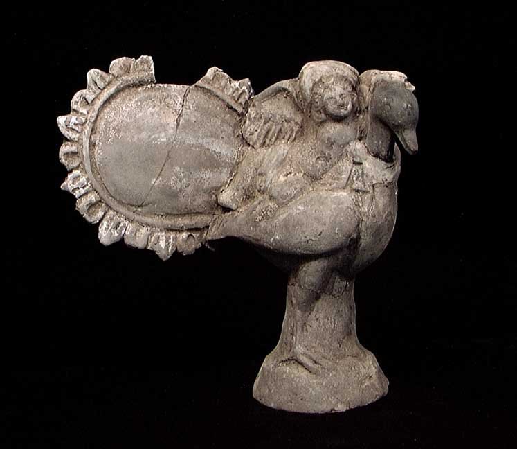 GREEK TERRA COTTA FIGURE OF EROS RIDING A PEACOCK: TERRA COTTA FIGURE OF EROS RIDING A PEACOCK. Greece, c. 4th-3rd century BC. With a nude Eros reclining on the back of a large peacock, a large mirror to the left. 5.5 x 5.5". A rare and charming figur