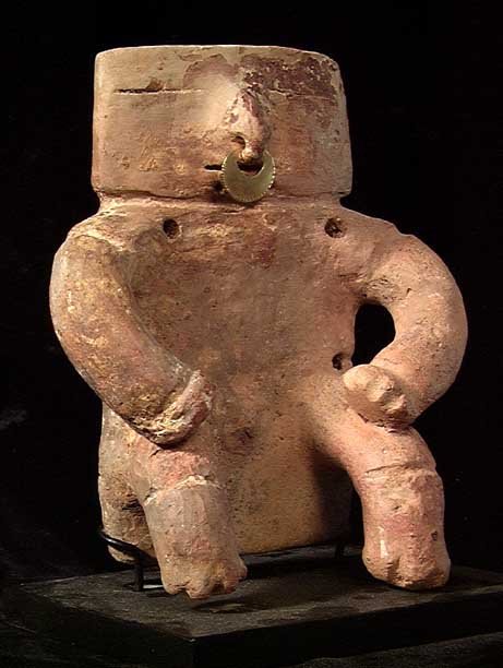 CHOICE QUIMBAYA SLAB FIGURE: QUIMBAYA SLAB FIGURE. Caldas complex, ca. 1000-1400. Heavy solid slab seated male figure with slit eyes and mouth, arms to knees. 5 x 6 inches. Cf. Labbe.74,82,83 for the general type. On custom stand