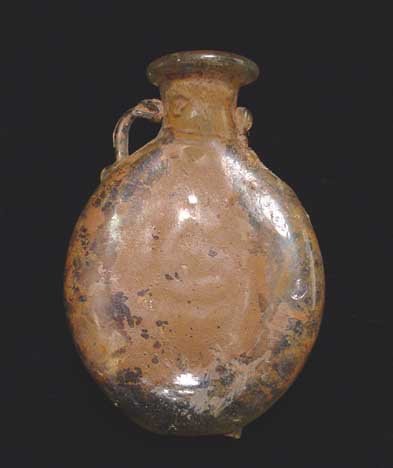 BYZANTINE GLASS PILGRIM BOTTLE: BYZANTINE GLASS PILGRIM BOTTLE, c. 4th-6th century AD. Flattened oval vessel with wide neck and twin small handles (one broken). Would likely to have been used to carry holy water. 2 x 2.75 inches. Sc