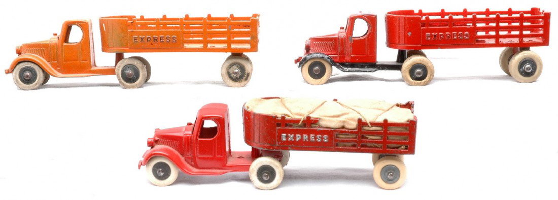 TootsieToy three 0801 Mack Express Stake Trucks: TootsieToy three 0801 Mack Express stake trucks, one red and one orange with six wheels and a truck that has black fenders with ten wheels. The trucks are C6-7.